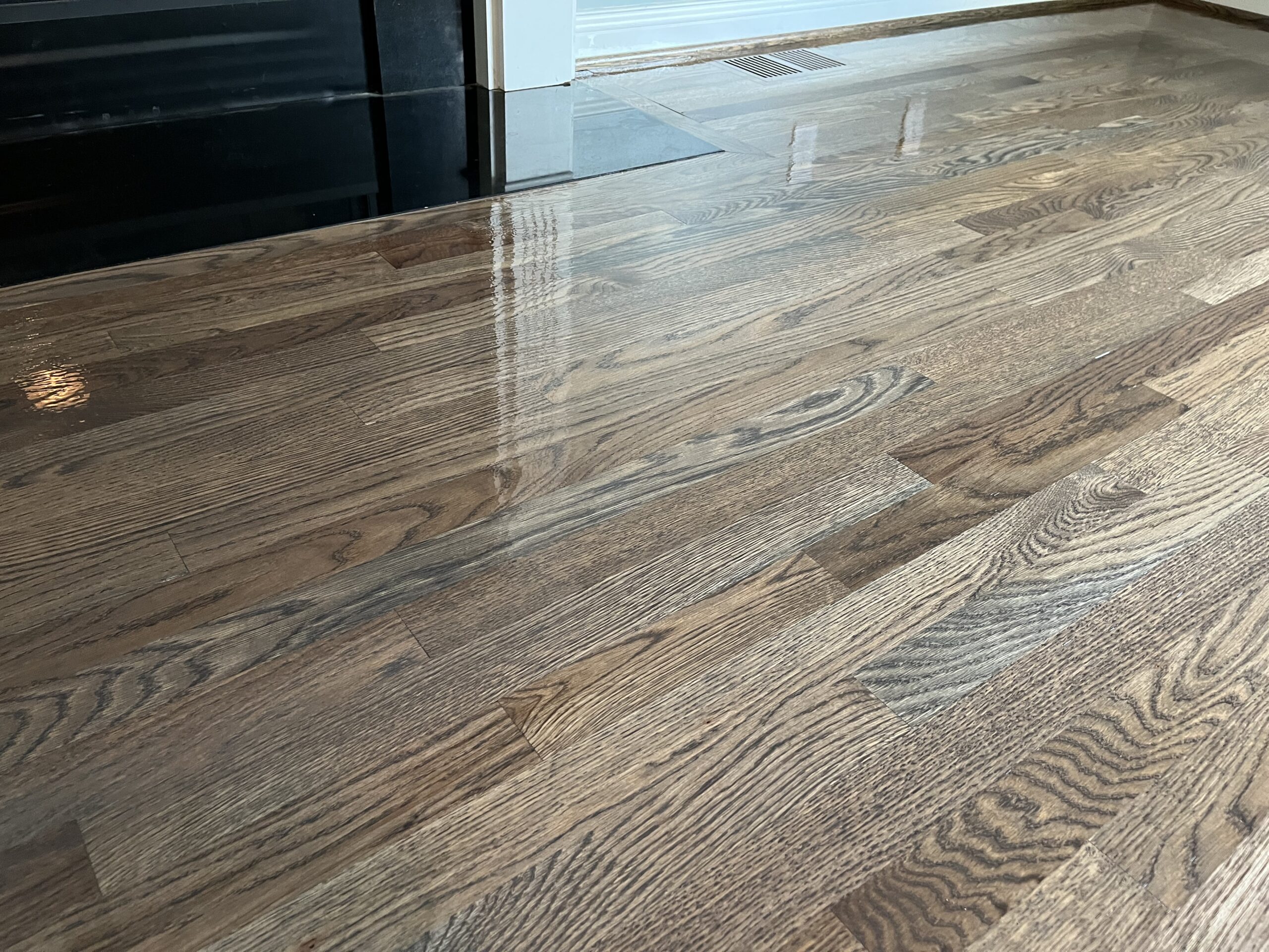 Glossy hardwood floor with a natural wood grain finish near a fireplace and a floor vent in a residential setting.