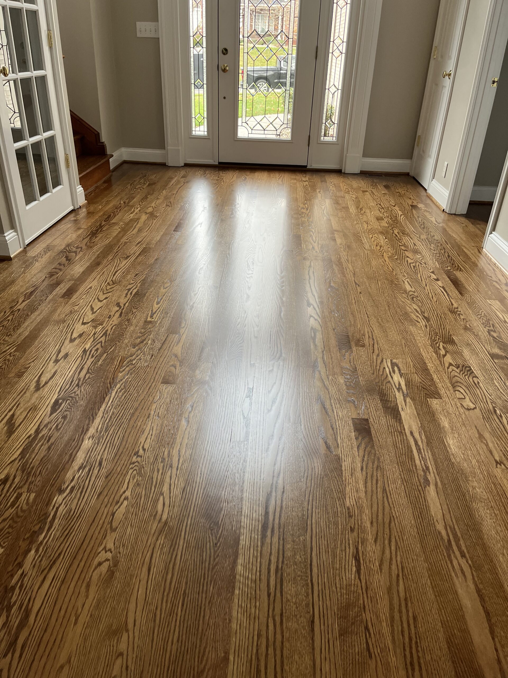 A room with polished hardwood floors, light tan walls, French doors on the left, and a glass-paneled front door letting in natural light.